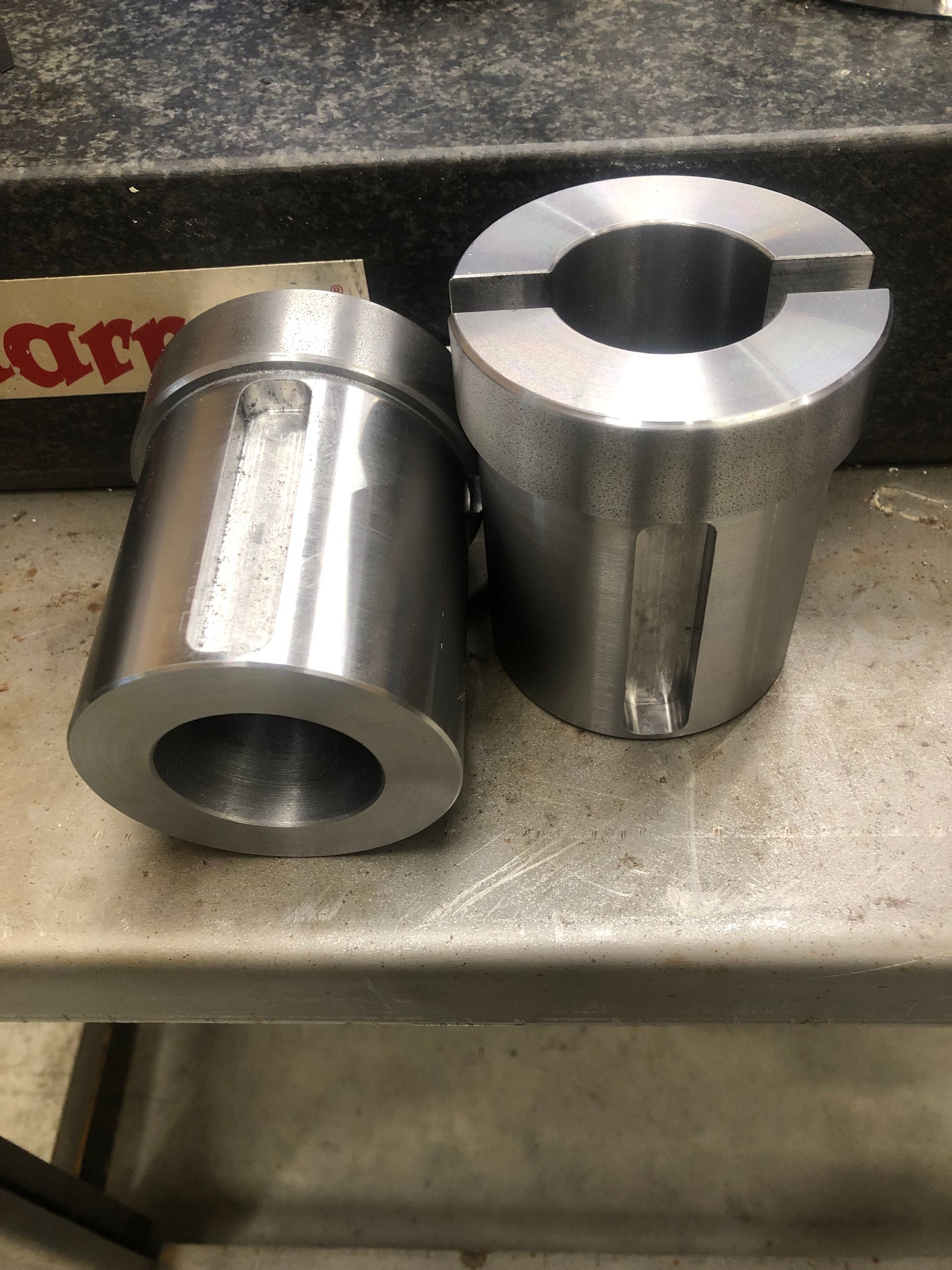 Two shiny metal machined cylinders on a workbench, one lying down and one standing upright.