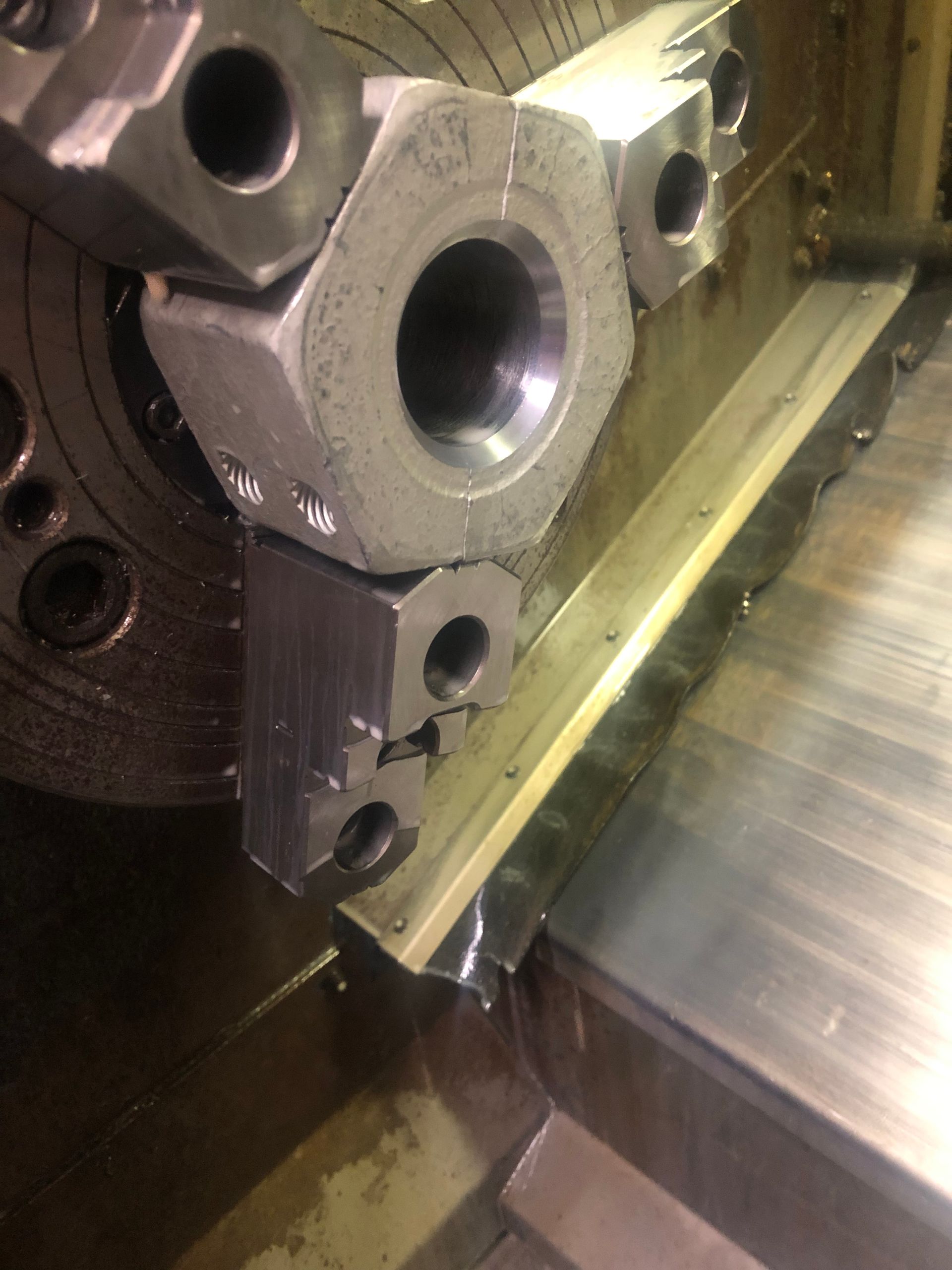 Close-up of a metal machine part with drilled holes and a cutting tool in a lathe or milling setup.