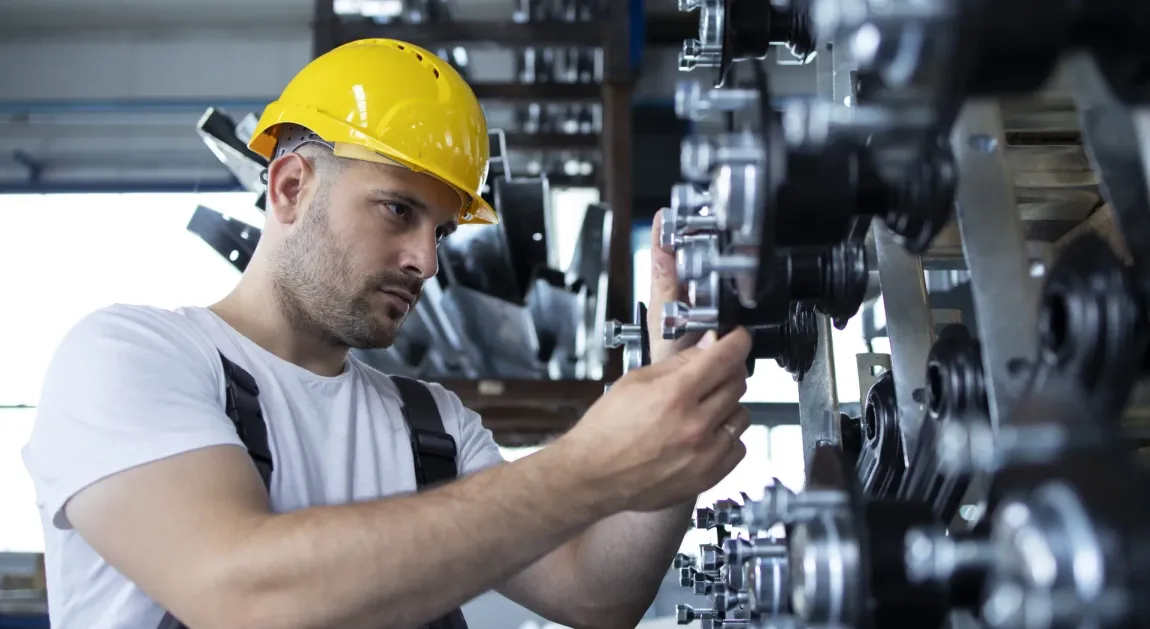 Worker in a yellow hard hat inspecting machinery in an industrial workshop