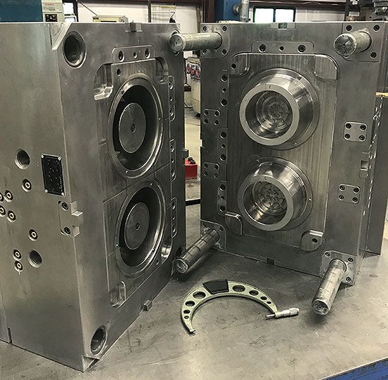 Open metal mold halves on a workbench, with circular cavities and machined parts in a factory setting