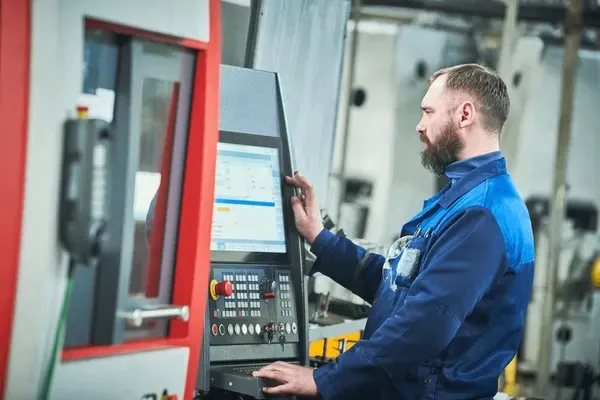Technician in blue workwear operating a control panel beside industrial machinery.