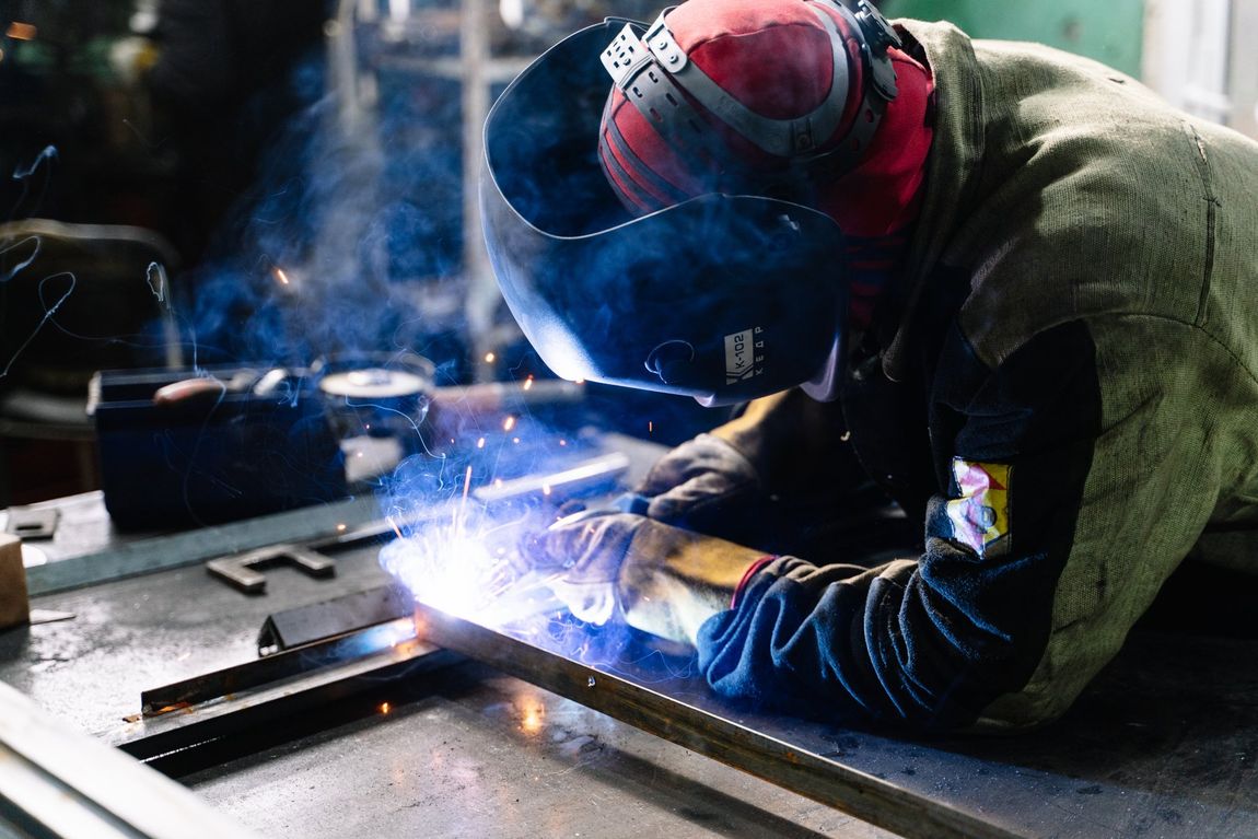 Welder in protective gear working on metal with bright sparks in an industrial workshop