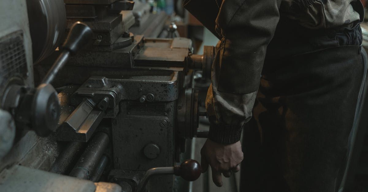 Person standing beside a large industrial machine, hand on a control lever in a dim workshop.